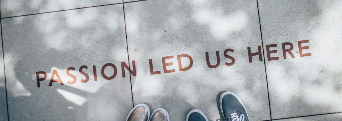 „Passion led us here“ Text auf dem Boden: „Passion led us here“ mit Schuhen im Vordergrund.