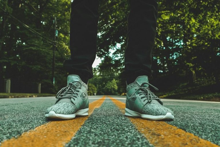 Graue Sneakers stehen auf einer Straße mit orangefarbenen Streifen und Bäumen im Hintergrund.