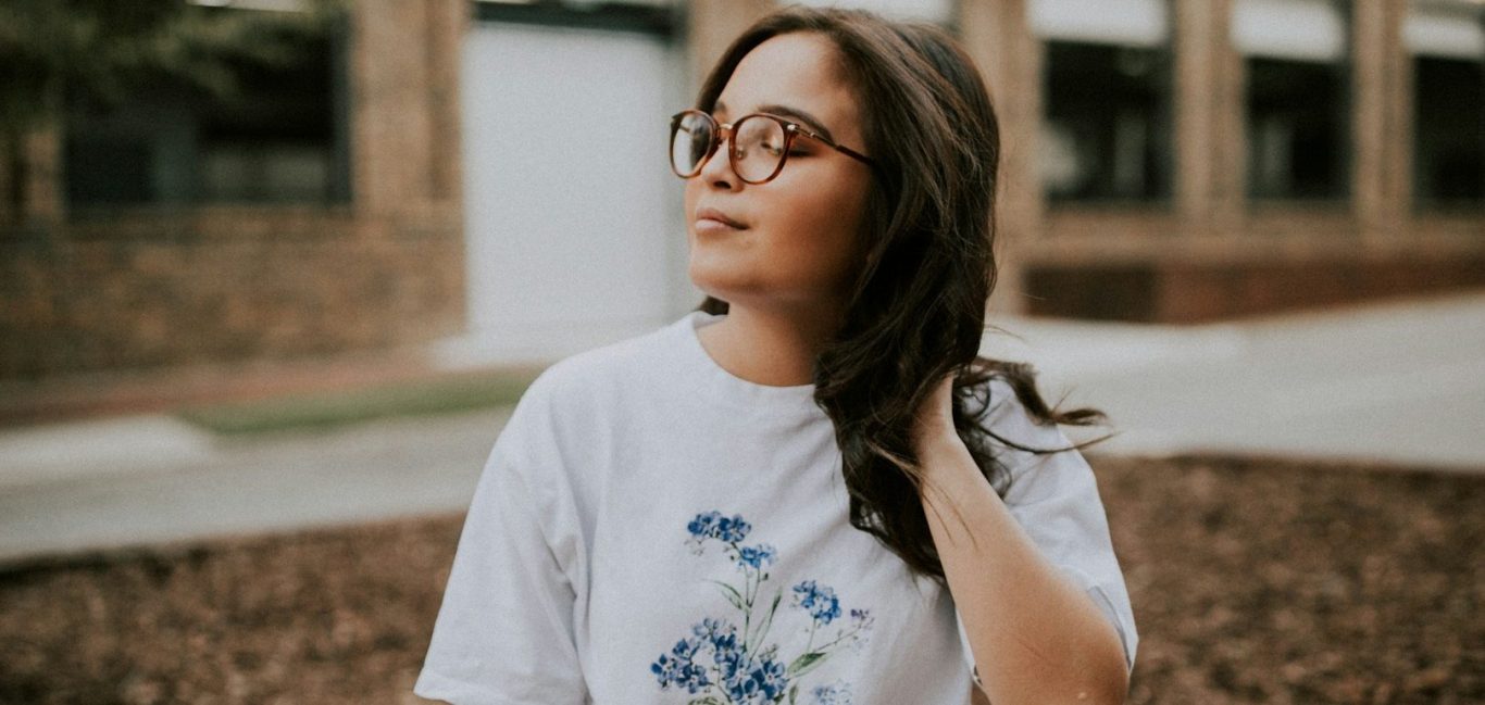 Junge Frau mit Brille und lockigem Haar Junge Frau mit Brille und lockigem Haar, trägt ein weißes T-Shirt mit floralem Muster.